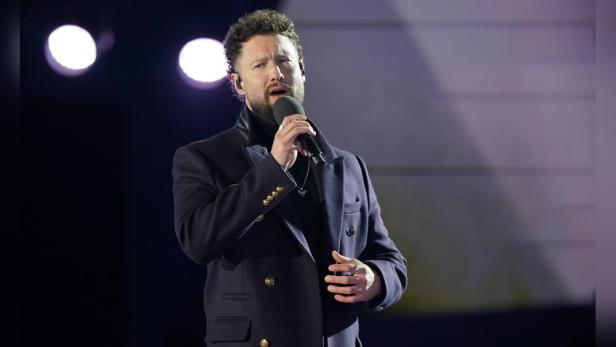 Der Popstar Calum Scott singt in ein Mikrofon.