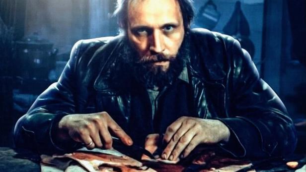 Ein Mann, vermutlich Karl Denke, sitzt an einem Tisch und schneidet Fleisch.