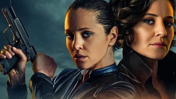 Das Filmplakat für „In From the Cold“ zeigt zwei Frauen, von denen eine eine Waffe hält, vor einer Skyline.