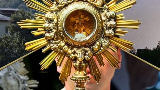 Eine Monstranz wird von einem Priester gehalten, während Gläubige im Hintergrund beten.