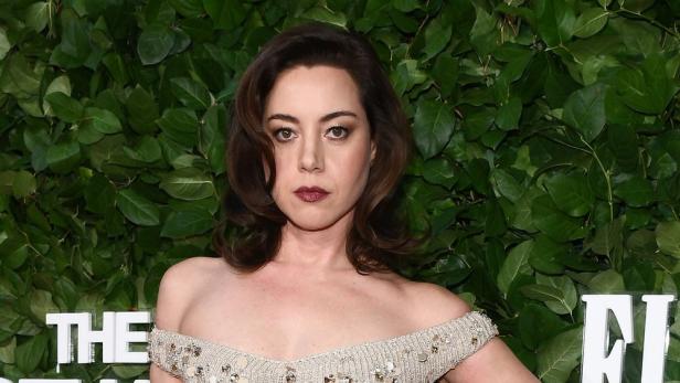 Schauspielerin Aubrey Plaza bei Presseempfang vor Wand aus grünen Blättern.