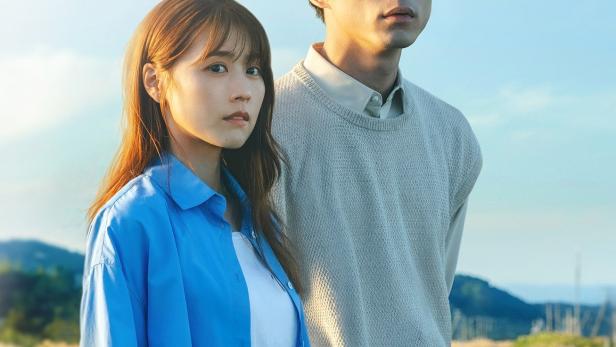 Ein junges Paar steht vor einer Landschaft mit Bahngleisen.