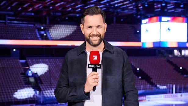 Moderator Matthias Killing steht mit Mikro in der Hand vor leerem Sportstadium.