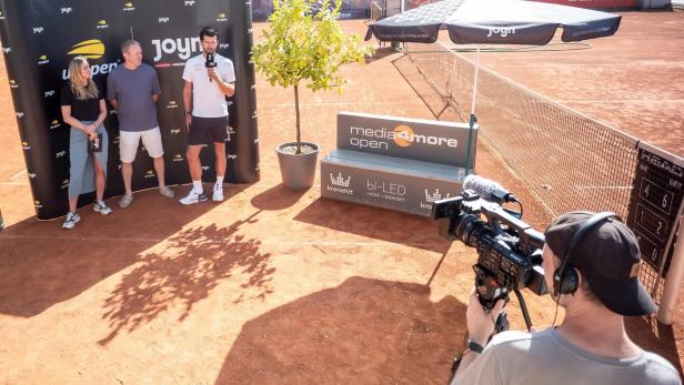Die JOYN-Sportmoderatoren-Crew wird auf einem Tennisplatz von einem Kameramann gefilmt.