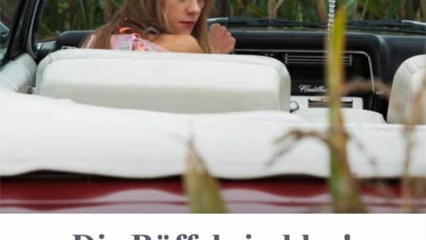 Eine Frau sitzt in einem roten Cadillac Cabrio vor einem Maisfeld.