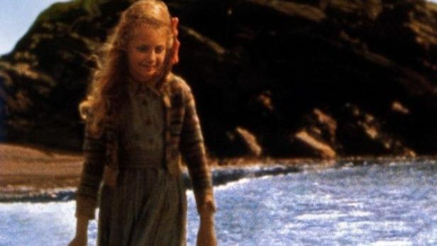 Eine junge Frau steht am Strand vor einem Seehund; Filmposter „Das Geheimnis des Seehundbabys“.