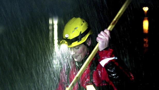 Ein Mitglied des „Storm Squad“ watet im Regen mit einem Stab durch das Wasser.