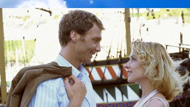 Ein Mann und eine Frau sehen sich verliebt an, im Hintergrund ein Schiff.