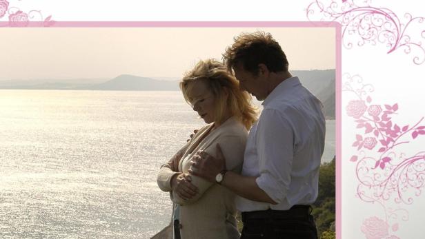 Ein Paar umarmt sich vor einer Küstenlandschaft im Stil von Rosamunde Pilcher.
