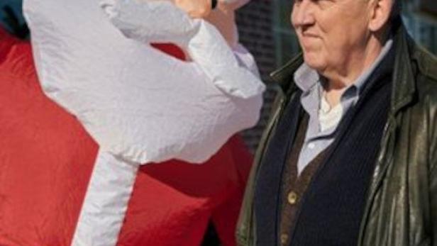 Ein Mann steht neben einer aufblasbaren Weihnachtsmann-Figur.