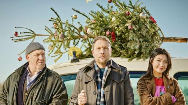 Das Filmplakat zu „Ein Taxi zur Bescherung“ zeigt Dietmar Bär, Max Riemelt und Nhung Hong vor einem Taxi mit Weihnachtsbaum.