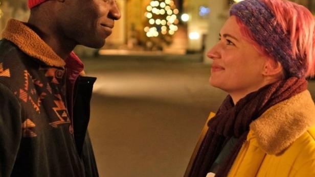 Ein Mann und eine Frau stehen sich vor einem Weihnachtsbaum an und lächeln sich an.