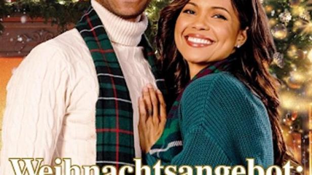 Ein lächelndes Paar umarmt sich vor einem Weihnachtsbaum, im Hintergrund ein Kamin mit Dekorationen.