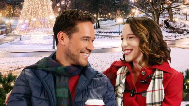 Ein Paar sitzt auf einer Bank vor einem beleuchteten Weihnachtsbaum im Film „Hot Chocolate Holiday“.