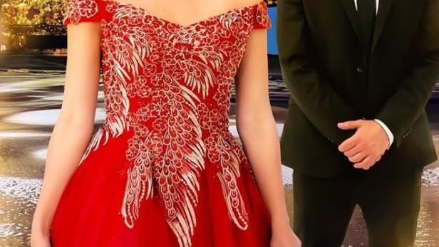 Eine Frau in einem roten Kleid und ein Mann im Anzug vor einem festlichen Gebäude für „A Model Christmas“.