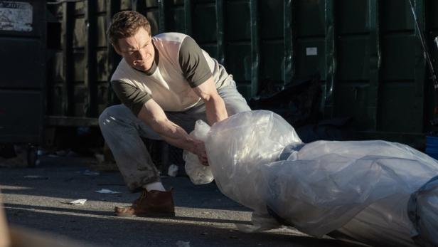 Patrick Gibson als junger Serienkiller Dexter schleift eine in Plastik verpackte Leiche hinter sich her.