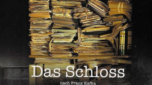 Das Filmplakat für „Das Schloss“ zeigt einen Stapel Akten und drei Personen im Dunkeln.