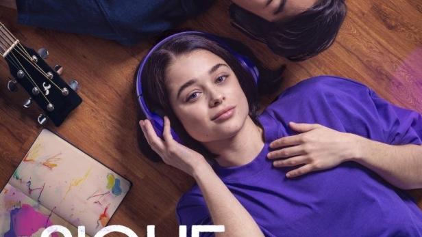 Ein junges Paar liegt auf dem Boden, Kopf an Kopf, während sie Kopfhörer tragen.