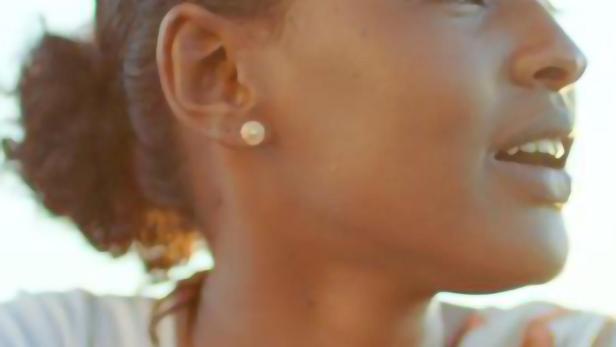 Eine junge Frau mit dunkler Haut und hochgesteckten Haaren schaut zur Seite.