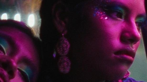 Eine Frau mit Glitzer-Make-up und Ohrringen im violetten Licht.