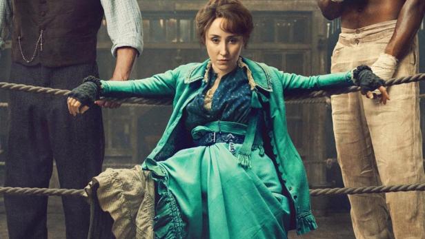 Das Filmplakat für „A Thousand Blows“ zeigt eine Frau zwischen zwei Männern in einer Boxarena.