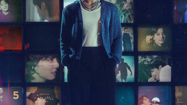 Jung Kook steht vor einer Wand aus Fernsehbildschirmen, die verschiedene Szenen zeigen.