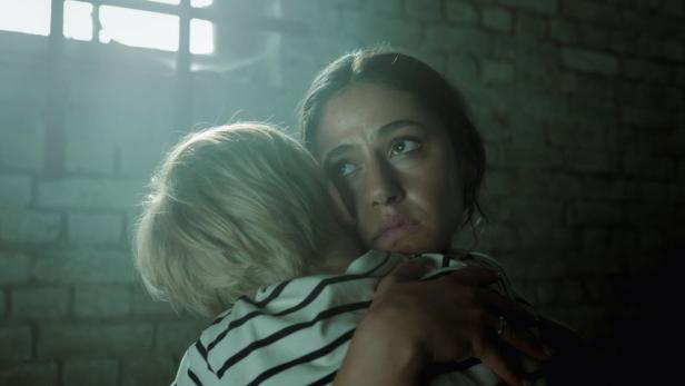 Frau drückt in düsterem Keller ihr Kind an sich.