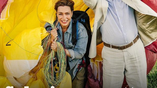 Das Filmplakat zu „Zimmer mit Stall – Schwiegermutter im Anflug“ zeigt zwei Personen vor einem Fallschirm.