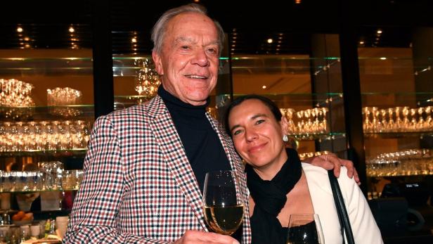 Dirk Galuba lehnt mit Weinglas in der Rechten und den linken Arm um Ehefrau Enrica an einer Bar.