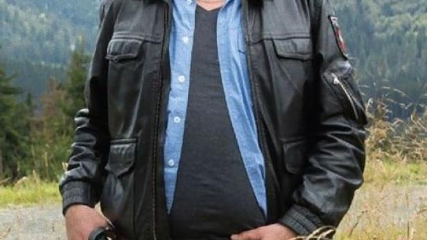 Ein Mann in Lederjacke steht vor einer Landschaft.