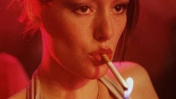 Eine Frau zündet sich in rotem Licht eine Zigarette an. Im Vordergrund steht das Wort „ALLEIN“.