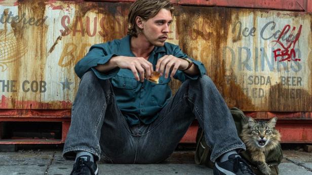 Austin Butler sitzt in „Caught Stealing“ auf dem Boden vor einem heruntergekommenen Lokal.