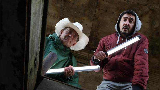 Wigald Boning und Eko Fresh beugen sich mit Leuchtstäben in Händen über eine Luke.