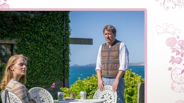 Ein Mann und eine Frau sitzen an einem Tisch im Garten; Filmposter „Liebe, Diebe, Diamanten“.