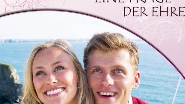 Ein lächelndes Paar hält Drachen vor einer Küstenlandschaft.