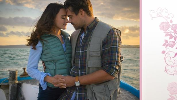 Ein Paar umarmt sich auf einem Boot vor dem Hintergrund eines Sonnenuntergangs.