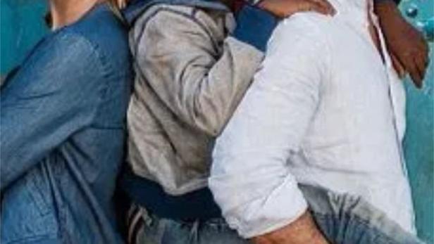 Ein lächelnder Junge steht zwischen einer Frau und einem Mann vor einer blauen Wand.