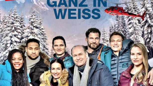 Das Filmplakat zu „In aller Freundschaft – Die jungen Ärzte: Ganz in Weiss“ mit dem Ensemble vor verschneiter Bergkulisse.