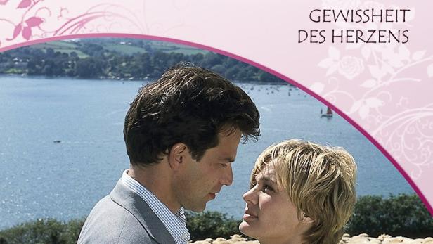 Ein Mann und eine Frau stehen sich vor einer Schafherde und dem Meer gegenüber, Titelbild „Rosamunde Pilcher – Gewissheit des Herzens“.