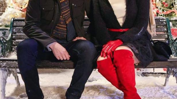 Ein Mann und eine Frau sitzen vor weihnachtlicher Kulisse auf einer Bank.