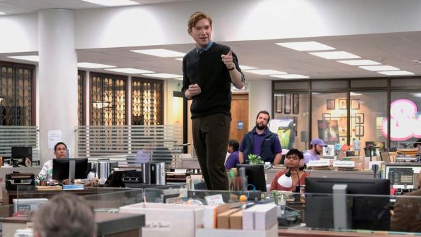 Domhnall Gleeson steht in seiner Serienrolle aus „The Paper“ auf dem Schreibtisch in einem Büro und spricht die Belegschaft an.