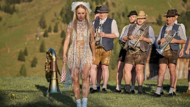 Luise von Finckh in ungewöhnlichem Braut-Outfit, während hinter ihr eine Blasmusikergruppe steht.
