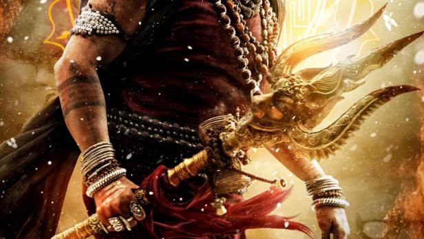 Ein Mann mit Bart und traditioneller Kleidung hält einen goldenen Dreizack.