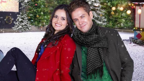 Ein Mann und eine Frau posieren vor dem Filmposter „Christmas at the Drive-In“.