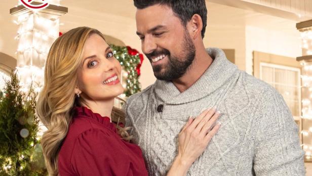 Ein Paar umarmt sich vor einem weihnachtlich geschmückten Haus, beworben als „Frühstück Weihnachten mit“.