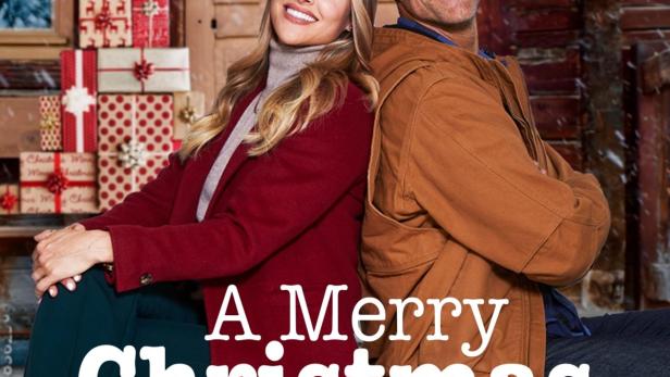 Ein Mann und eine Frau sitzen vor einer Holztür, die mit Weihnachtsschmuck verziert ist.