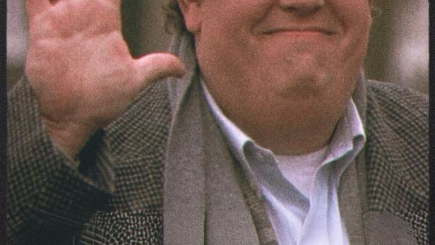 John Candy mit Hut und Schal winkt in die Kamera.