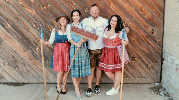 Vier „Bauer sucht Frau“-Kandidaten vor einer Hoftür mit Besen und Mistgabeln.