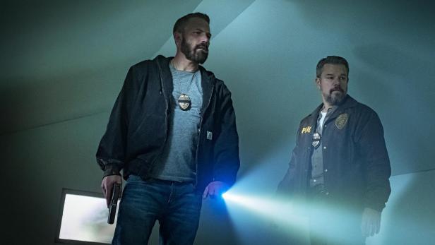 Matt Damon und Ben Affleck als Polizisten mit Dienstmarke, Taschenlampe und gezogener Waffe.