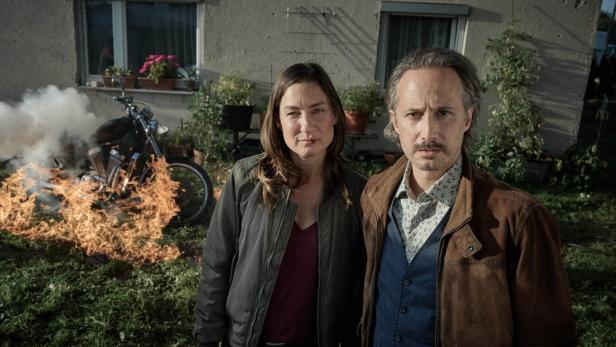 Marie Leuenberger und Michael Ostrowksi stehen als Ermittler im Garten vor einem brennenden Motorrad.